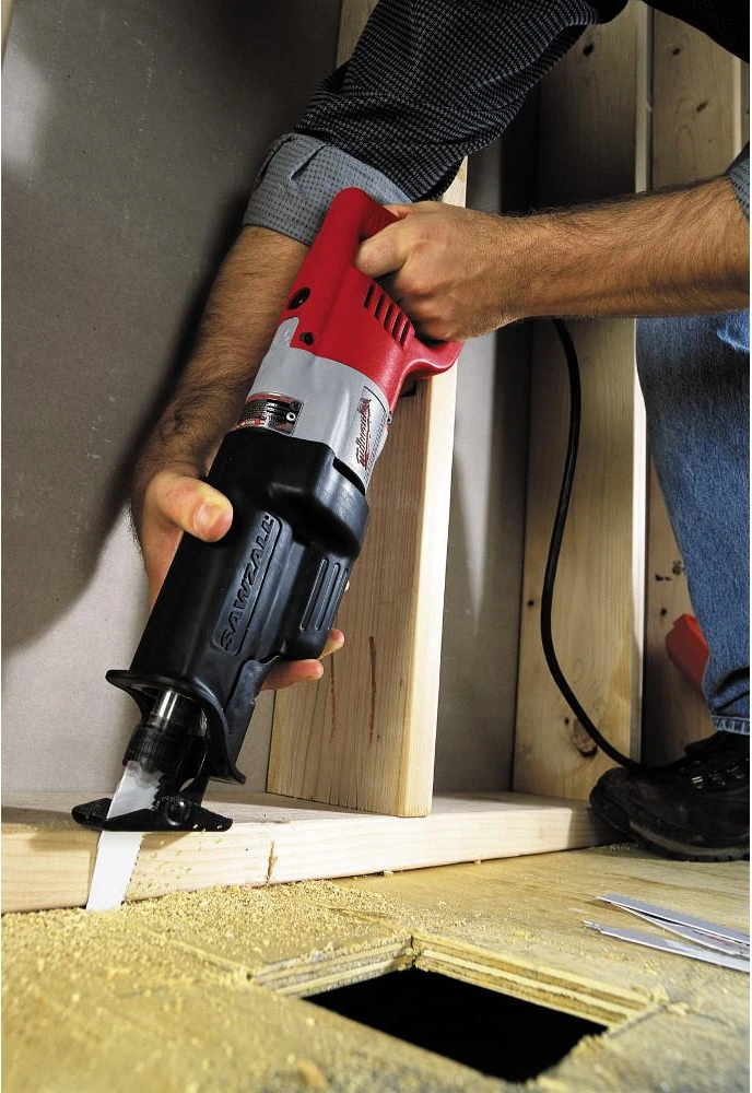 A worker cutting a subfloor with a Milwaukee reciprocating saw