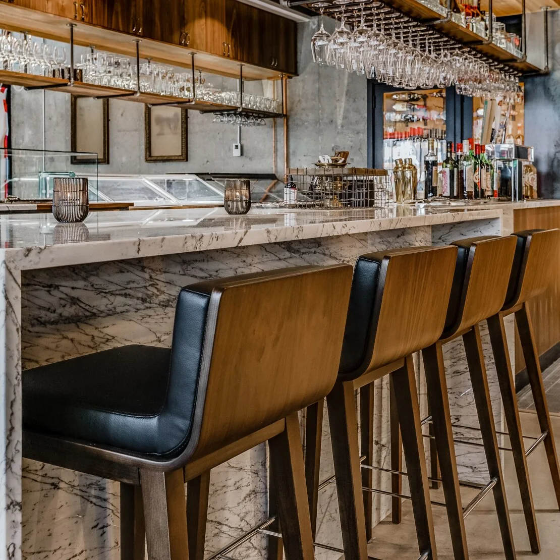 Veined stone surfaces and dark leather stools at a restaurant bar