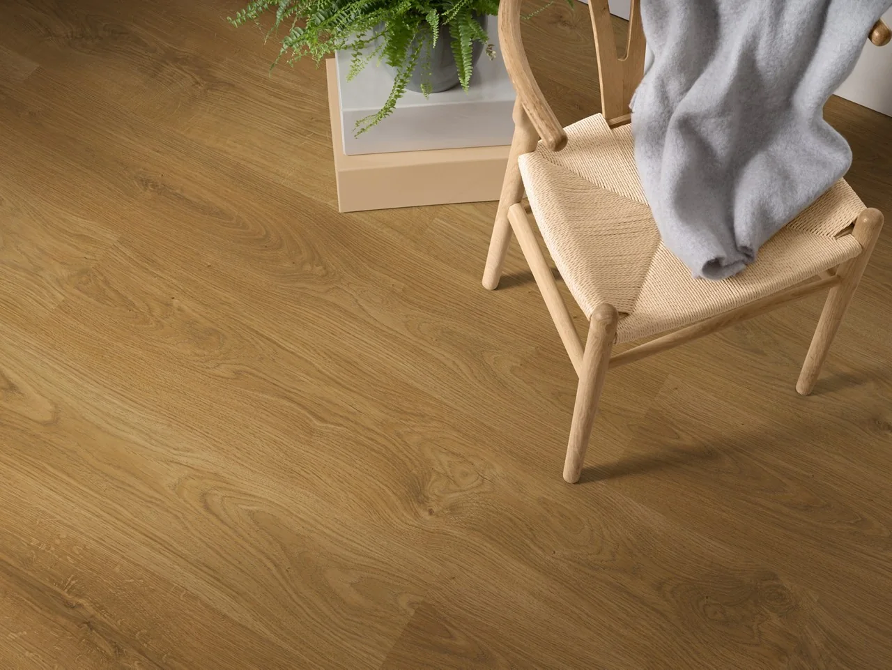 Warm oak-toned flooring beside a woven chair and green fern