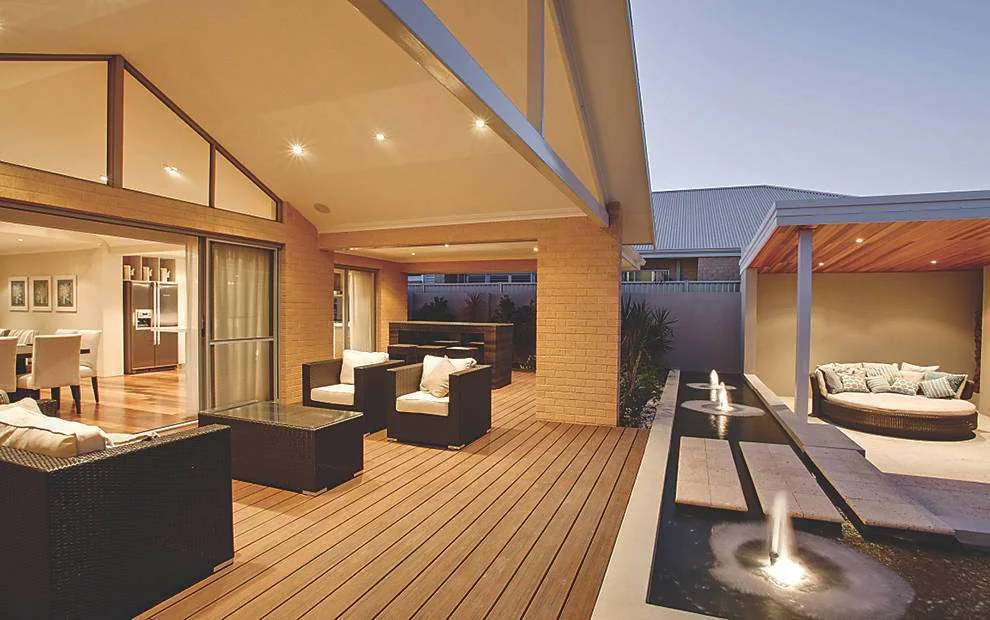 A warmly lit deck connects a glazed house and courtyard at dusk