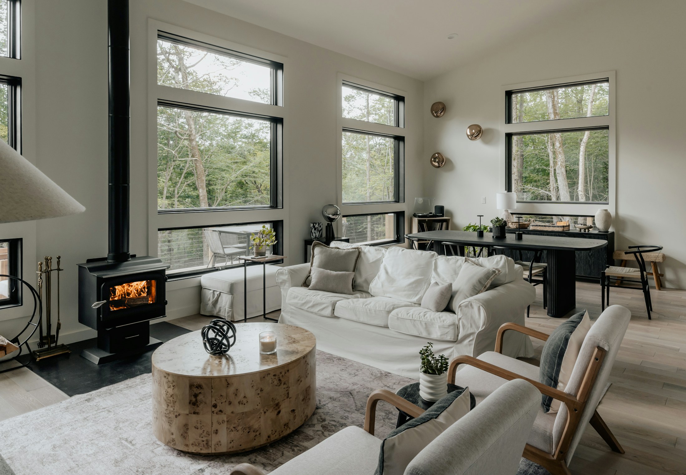 A bright living room with pale wood flooring, a white slipcovered sofa and a wood stove